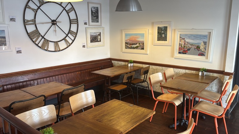 The seating room at Crumbs Kitchen with wooden tables and local artwork