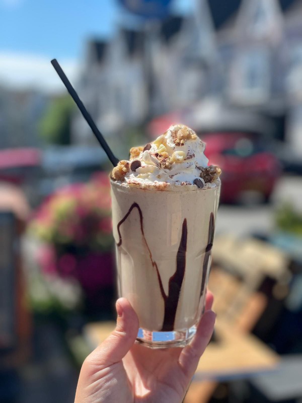 Milkshake with whipped cream, held up in the sunshine outside the café