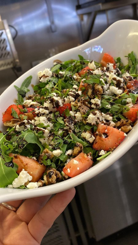 Strawberry, feta and rocket salad with balsamic glaze, held to the camera